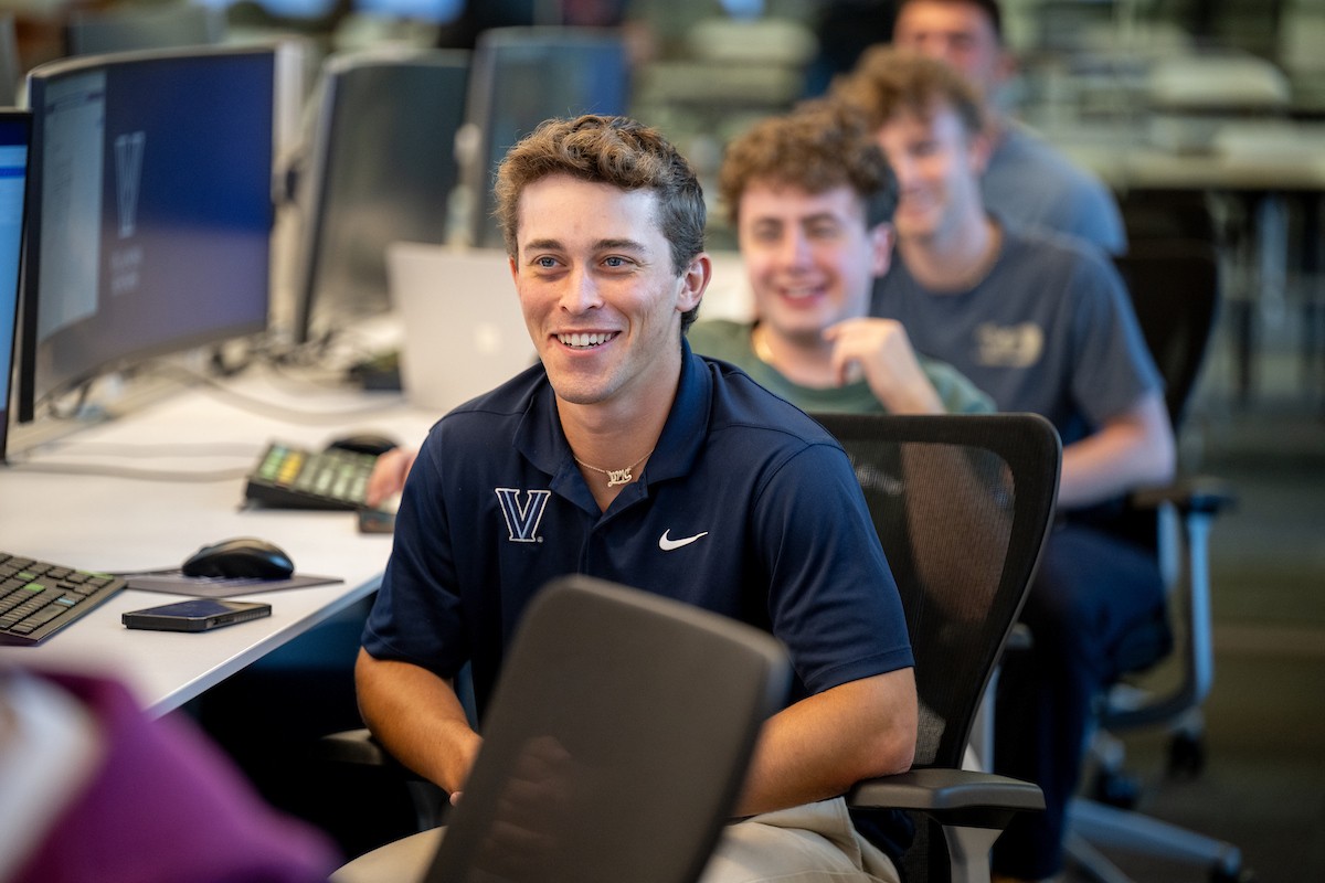 Students sitting at desks in a row, smiling and looking forward.