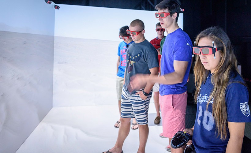 Students stand in a desert in the CAVE. image of students wearing VR glasses in front of a desert backdrop