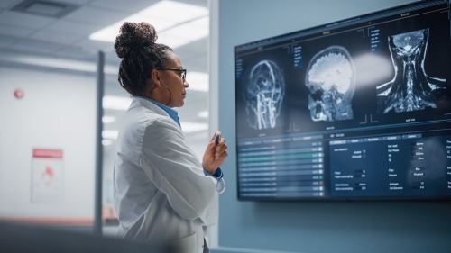 1388388697 Female in labcoat looking at medical images on screen