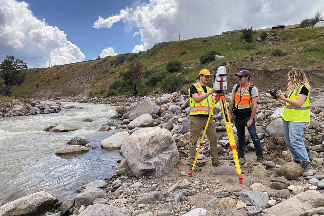 three people in safety vests survey the damage after historic flooding in Yellowstone National Park