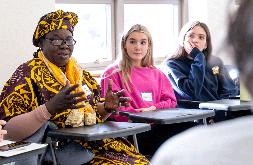 Dr. Margaret Itto sits at a desk in a classroom amongst Villanova students